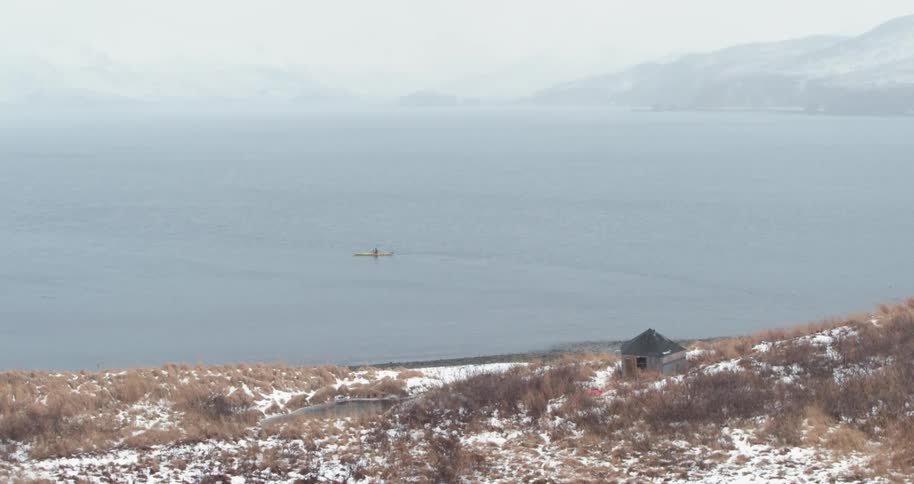 A person sits in a kayak just off shore on a winter day