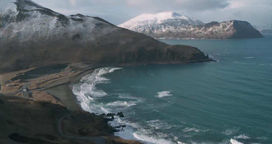 Ocean waves crash to shore surrounded by snowy mountains