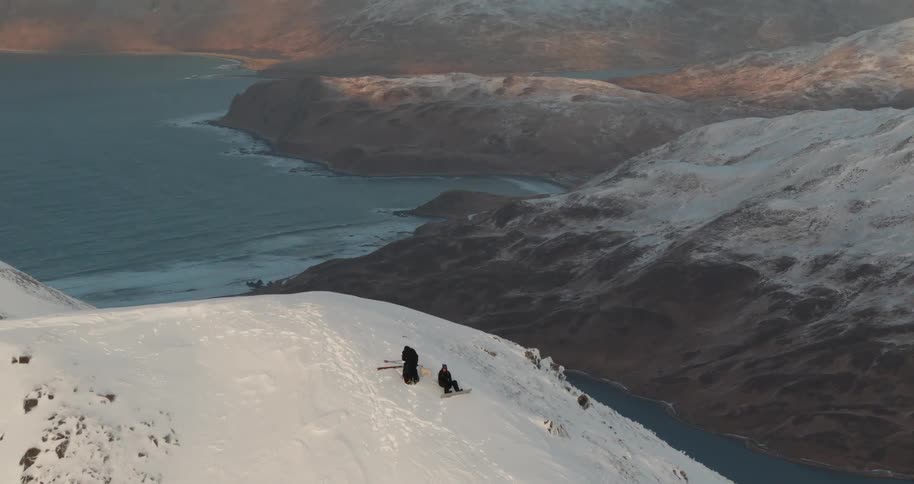 Two skiers rest on the top of a snow covered slope in front of the sea