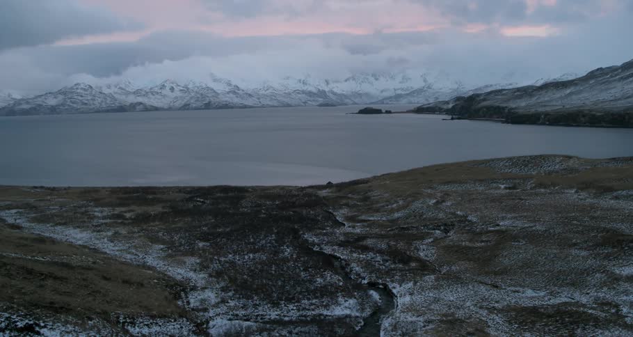 Snowy mountains surround water at sunset