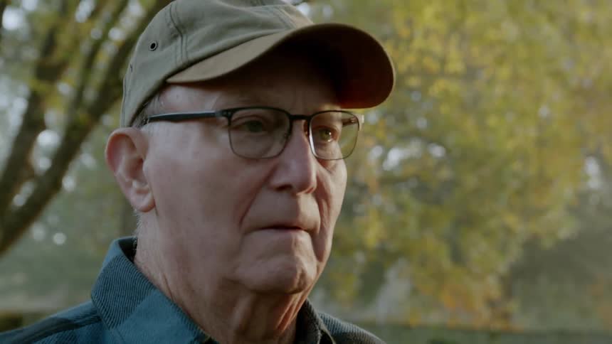 An old man is staring into the distance as he stands outside thinking