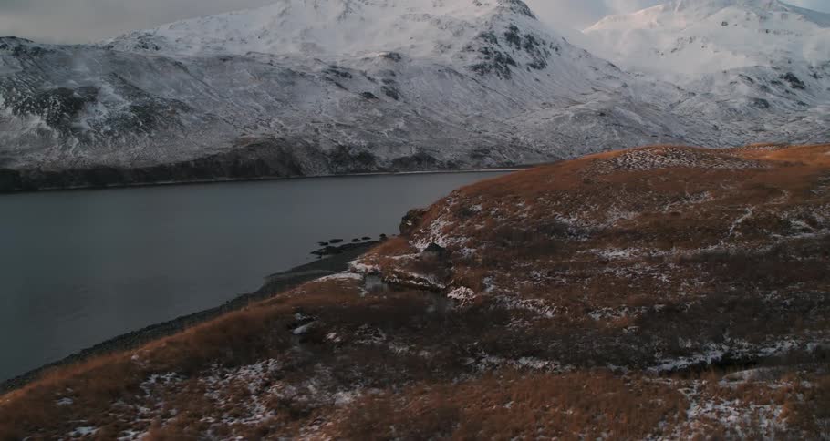 Clouds are casting shadows on snow-covered mountains on a remote coast