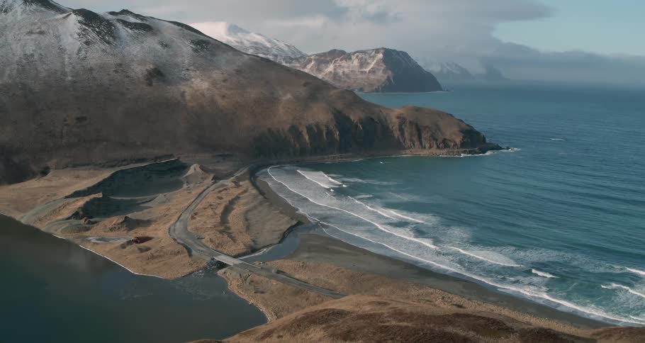 Waves meet the shore near snow capped mountains