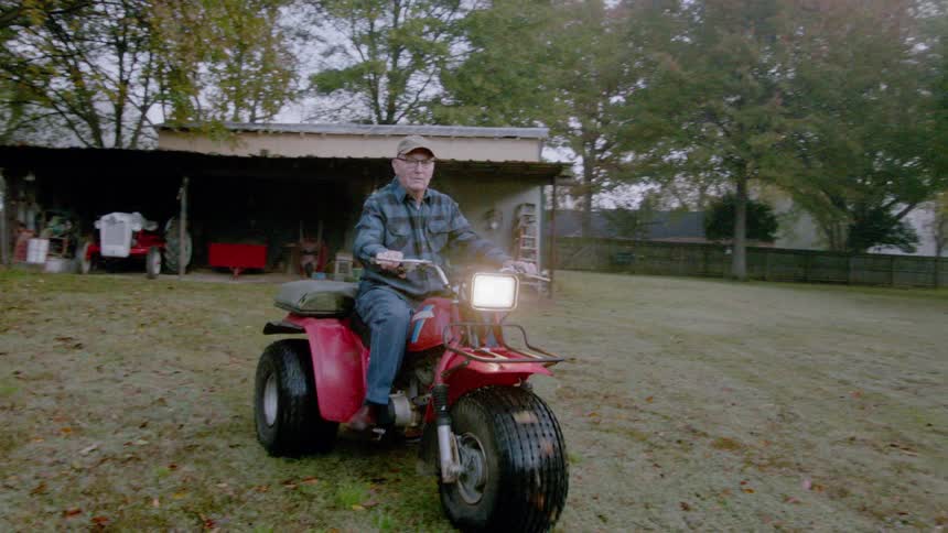 Older man riding a large three wheeler across a yard