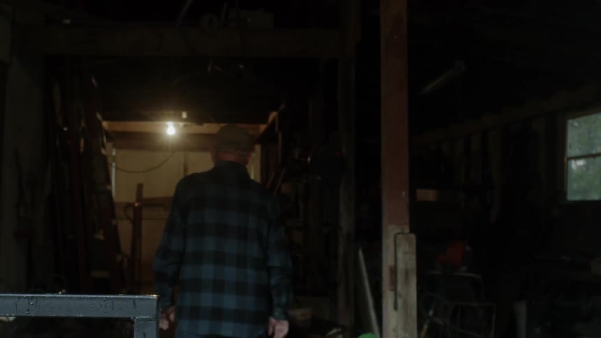 An older man is turning on a light and walking into a shed