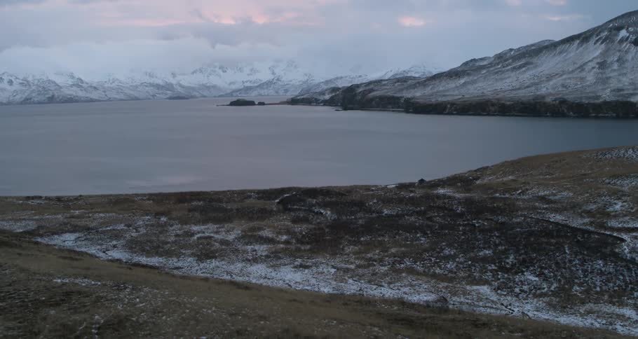 Snowy mountains surround water at sunset