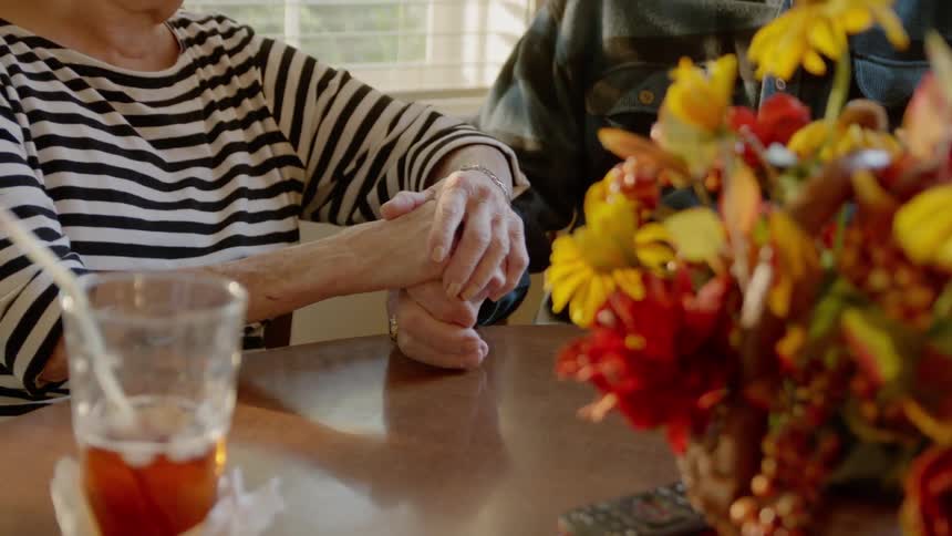 Two people are sitting at a table and holding hands talking