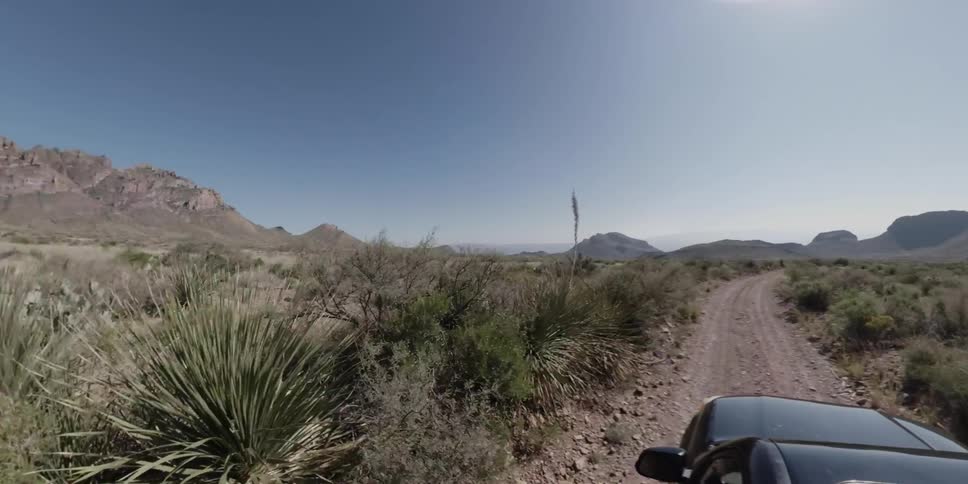 An suv is driving on a dirt road in the desert on a sunny day