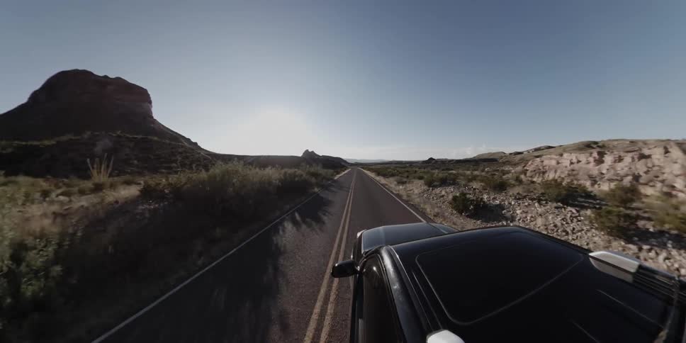 A car with a sunroof travels on a rural desert road on a sunny day
