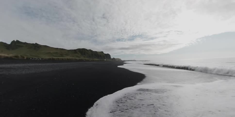 Small waves are crashing along a black sand shore line