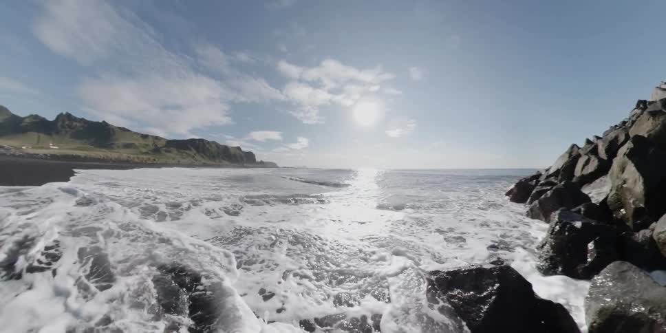 The tide crashes and rolls onto a rocky beach on a sunny day