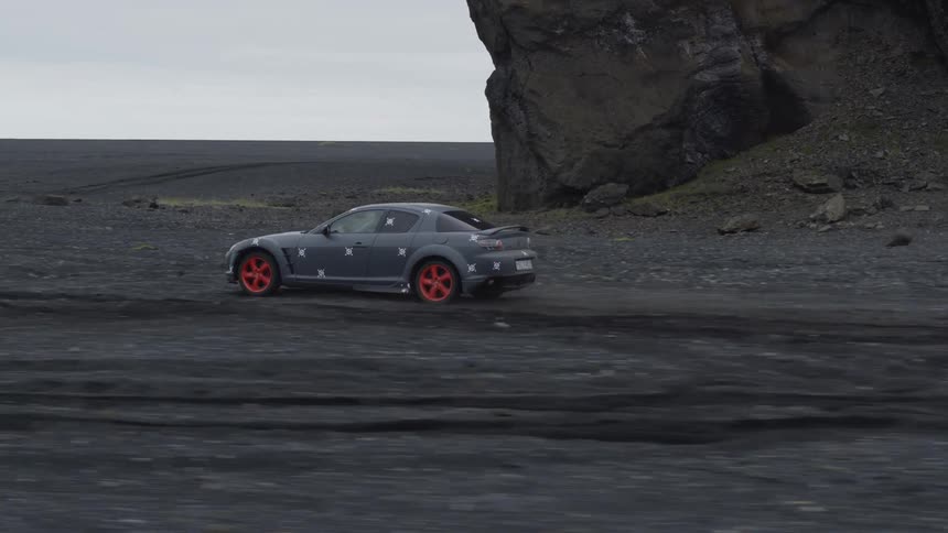 A rally car is driving really fast over a dirt and rock flatland