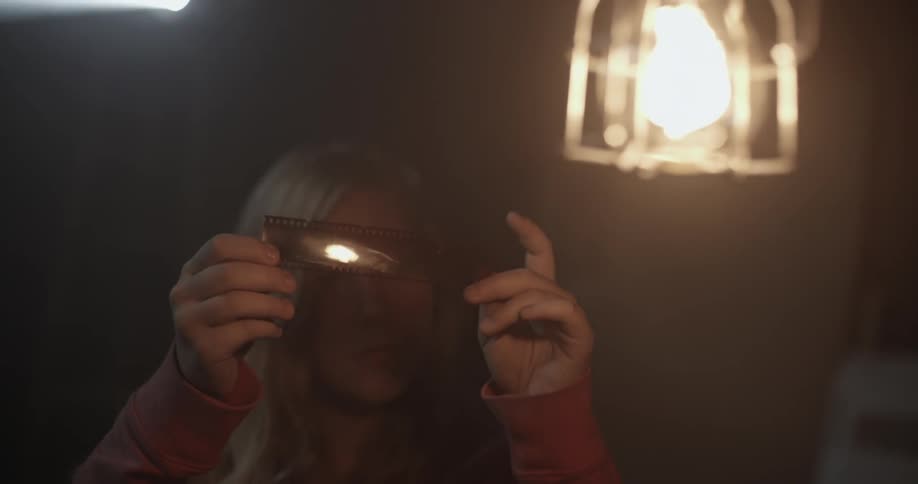 A woman is examining film in a dark room