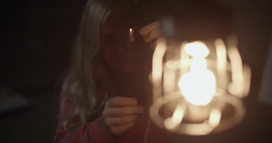 A woman holds something up to a lantern to inspect it