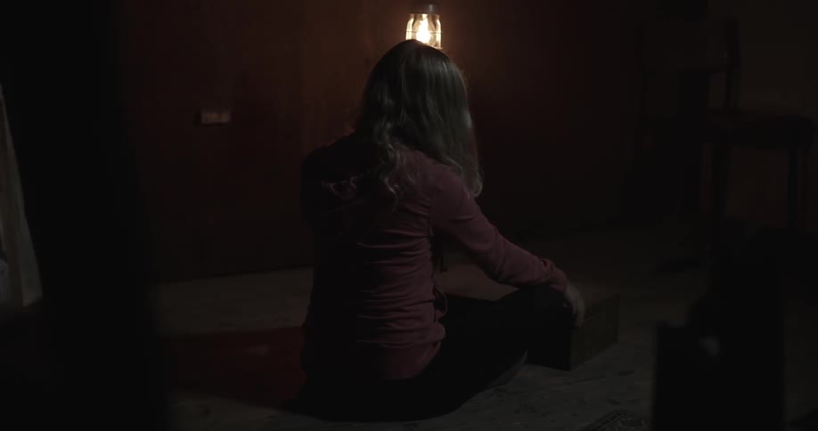 A woman is sitting in a dark room with only one small light