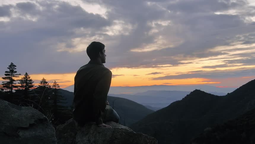 A man looks out over a mountain range at sunset