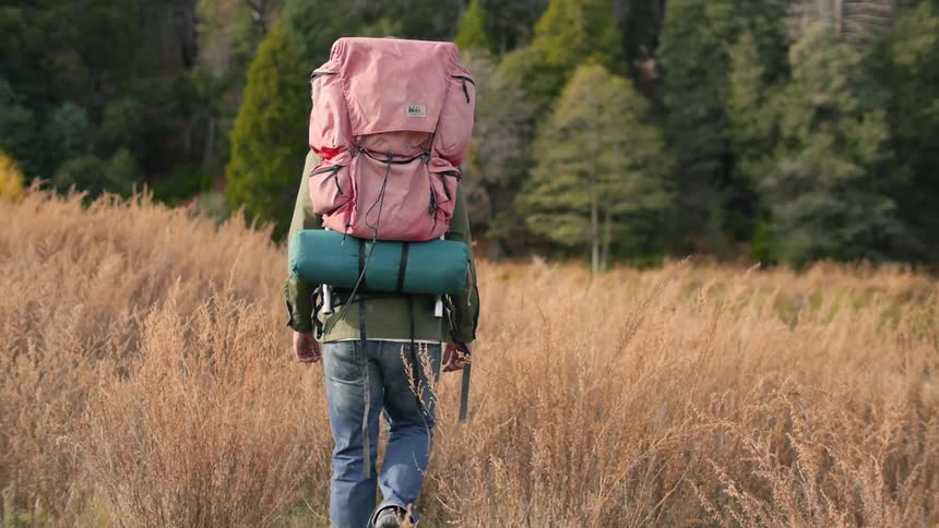 Woman hiking down a grass field towards a forest