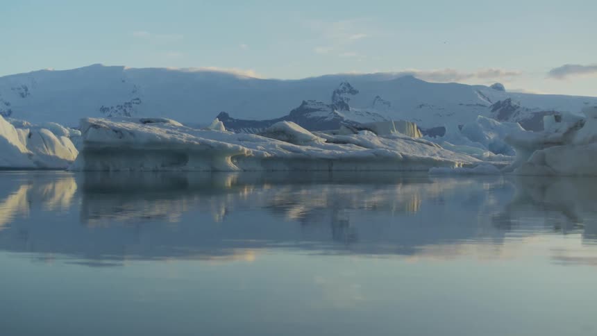 A coast with water and ice with snow covered land and the sky in the background