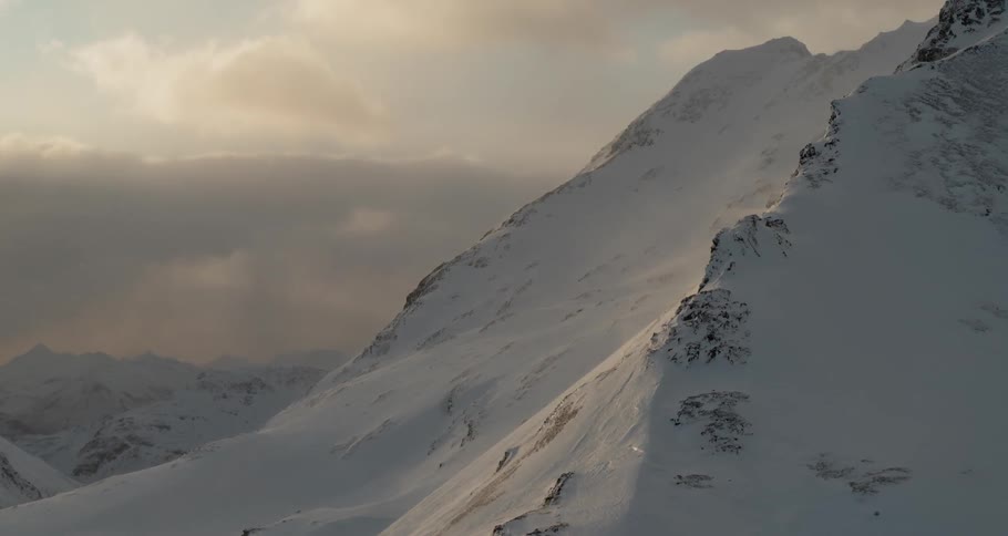 Clouds hover in the sky at dusk below a mountain peak in winter