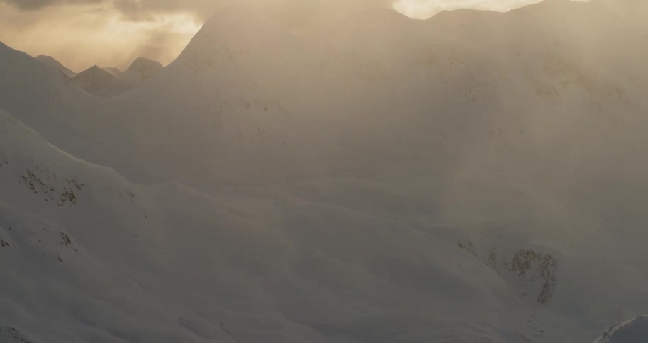 The sun sets over snowy mountains and blowing snow