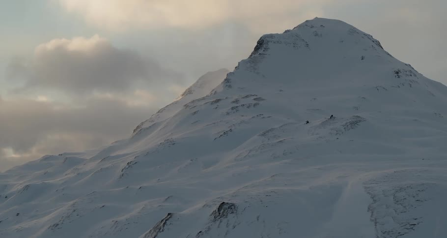 Clouds are drifting above a snow-covered mountain peak during the day