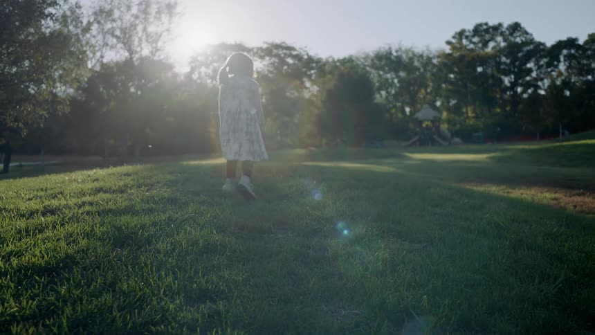 A young girl walks on grass on a sunny day
