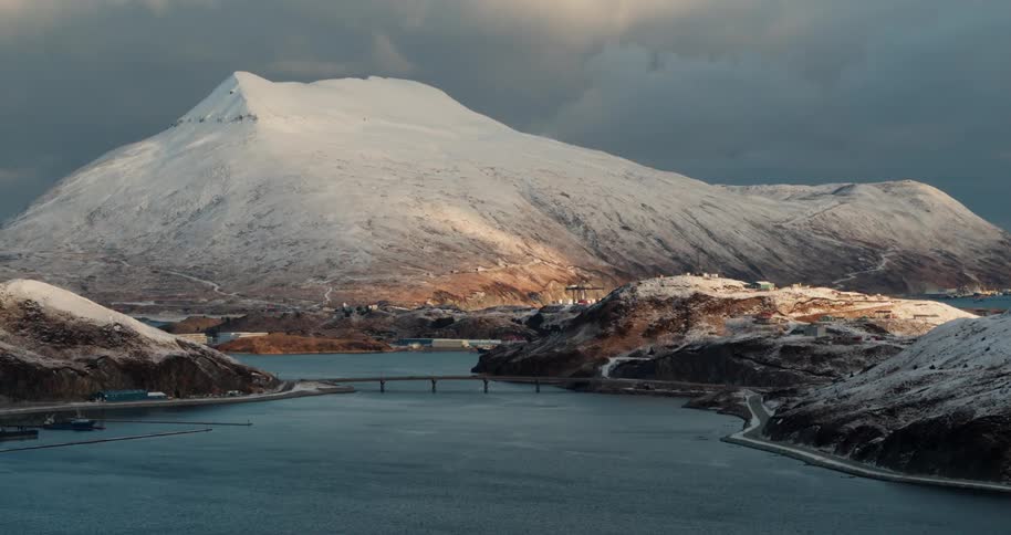 Bridge crossing water at the base of snow covered mountains