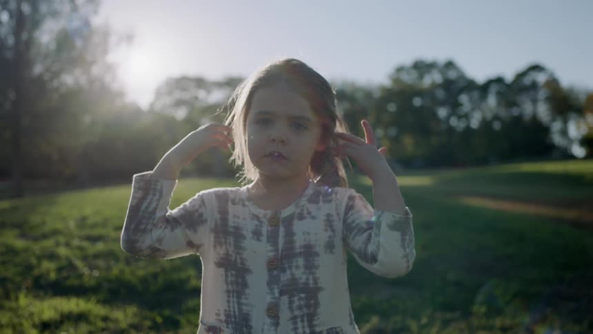 A young girl stands on grass on a sunny day