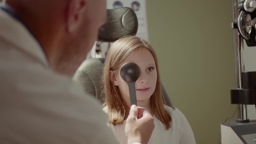 An optometrist is doing on eye exam on a girl in his office
