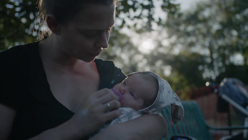 Woman holding and gently swaying a baby outdoors near sunset