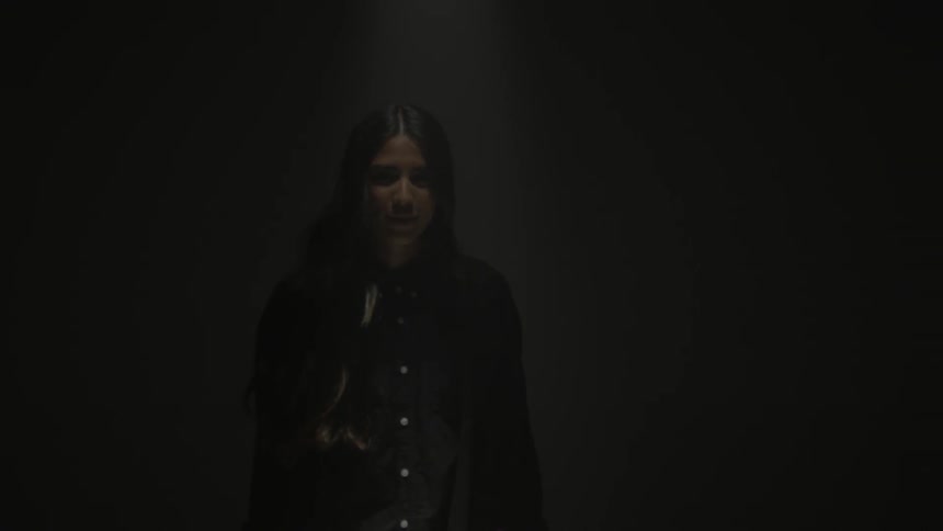 A woman standing in a room is raising a violin and preparing to play