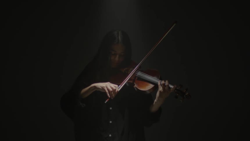 A musician plays the violin in a room with a black background