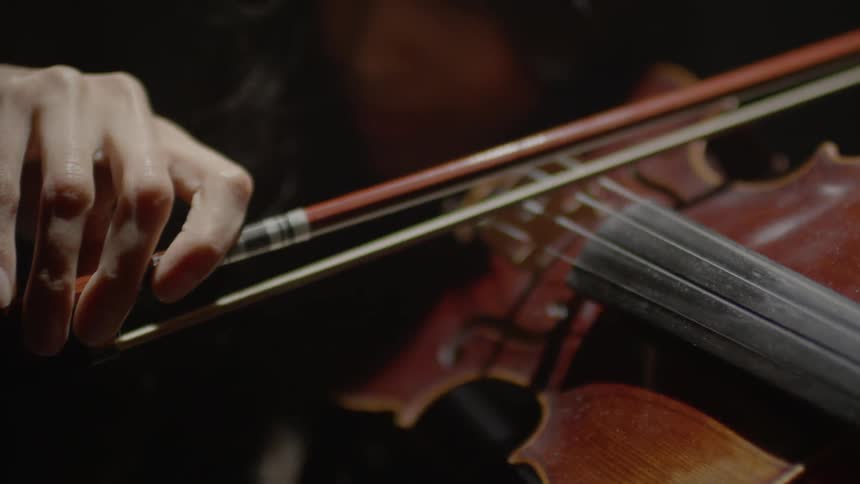 A bow is being pulled back and forth over a violin's strings