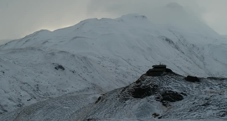 Storm clouds are hanging in the sky above snow-covered mountain peaks as a person looks on from a ledge