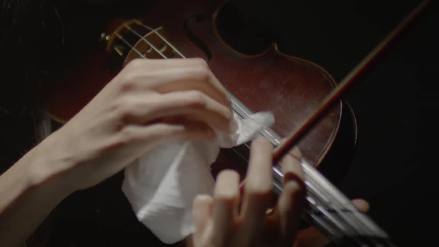 A violinists is rubbing the strings of her violin with a paper towel