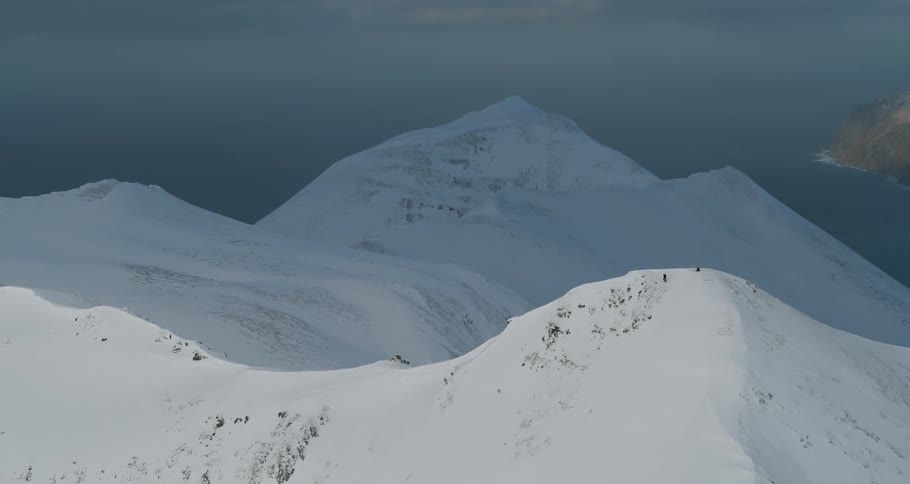 Two people stand on a snow covered mountain peak