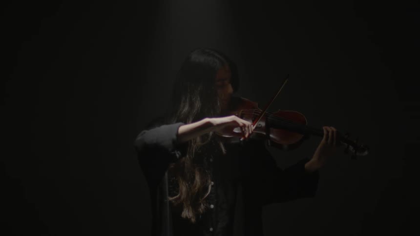 A woman plays a violin in the dark