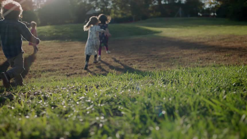 Children run down a hill on a sunny day