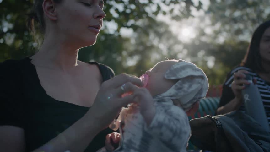 Woman sitting outside gives crying baby a pacifier