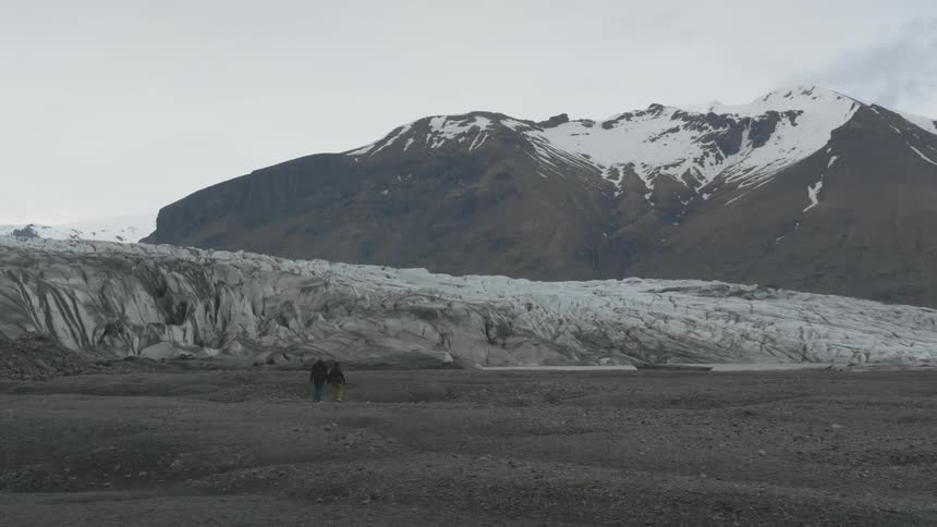 People walking across a field towards snowy mountains