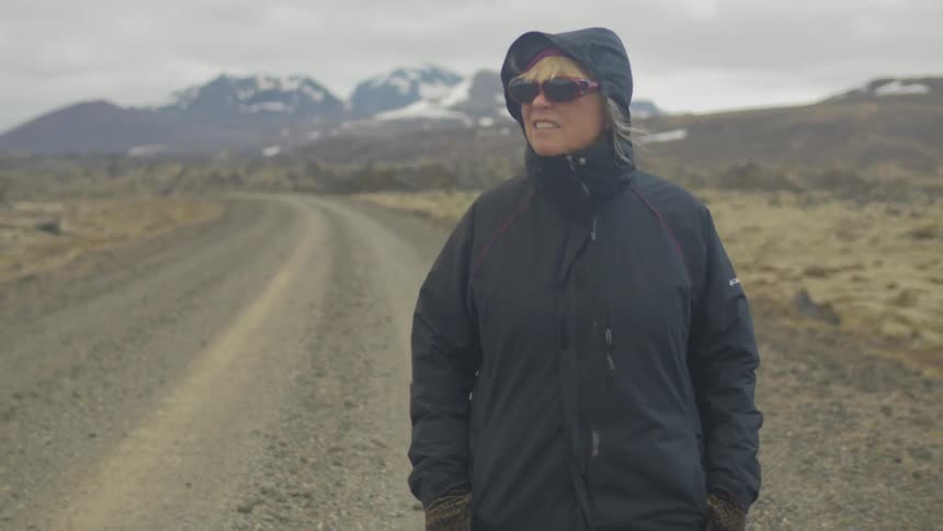 A woman walks along a dirt road wearing a heavy coat