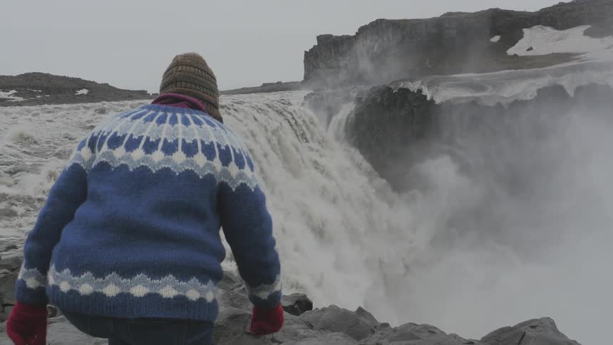 Person walks over some rocks towards the top of a large waterfall