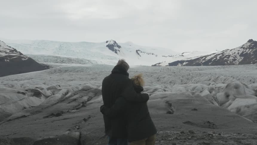 People hugging as they look at a snowy mountain range