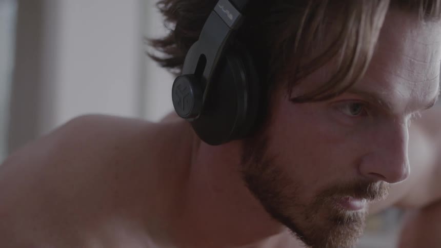 A shirtless man stretches while wearing headphones