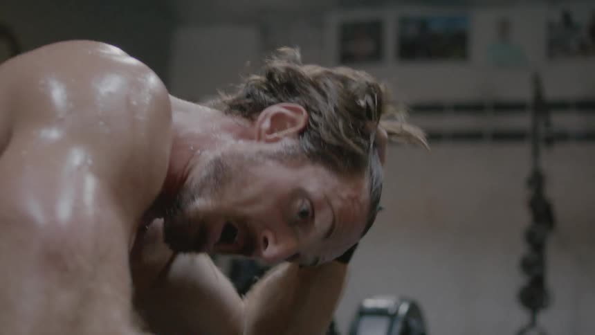 A man without a shirt is out of breath and sweating after working out in the gym