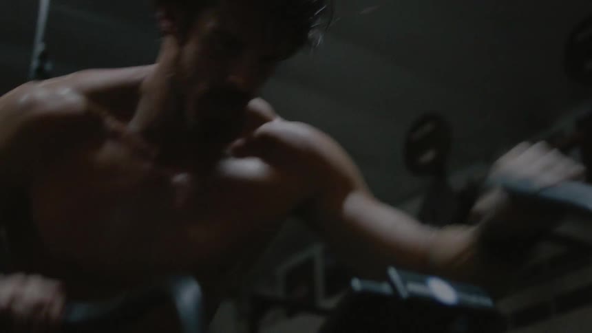 A man without a shirt is riding an exercise bike really fast in the gym