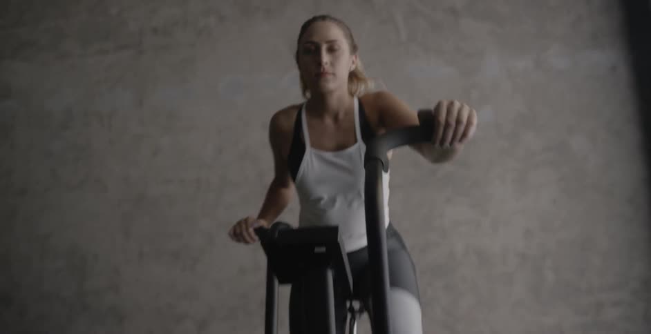 A woman is working out on a stationary bike in a gym during the day