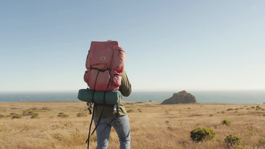 Person hiking on a grass field then climbs up on some rocks