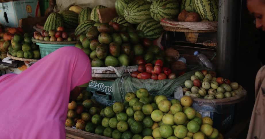 A woman selects fruit from a bin at a farmers market