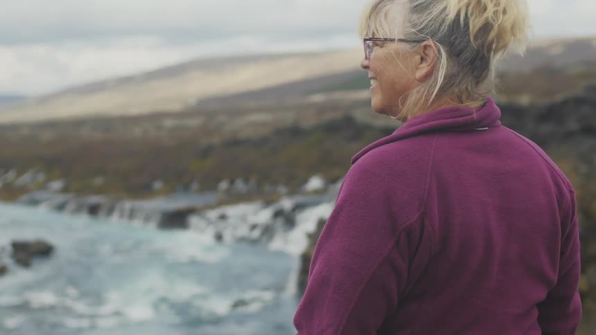 A woman smiles as she stands on a cliff overlooking the ocean